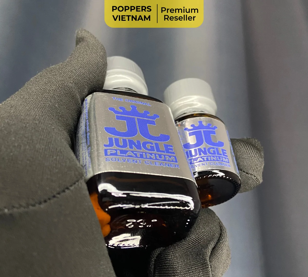 Hình ảnh là 2 chai popper Jungle Platinum 10ml và 30ml được Poppers Việt Nam chụp tại cửa hàng ở Hồ Chí Minh bằng máy ảnh kỹ thuật số, sản phẩm được nằm gọn gàng trên găng tay đen - sạch sẽ.