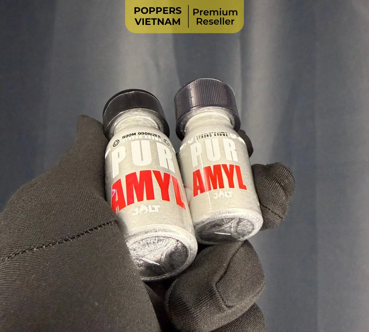 Hình ảnh là 2 chai popper Amyl 10ml và 25ml được chụp bởi Poppers Việt Nam. Chất liệu sản phẩm là chai nhôm bóng loáng kết hợp với găng tay đen tạo nên khung cảnh sạch sẽ.