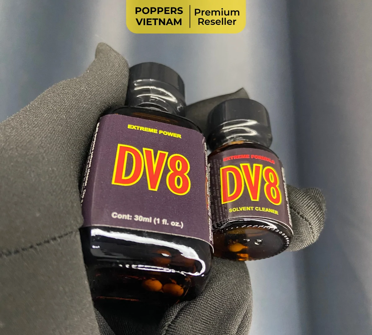 Hình ảnh cận cảnh 2 chai poppers DV8 với dung tích 10ml và 30ml được cầm tay bao tay vải, nền phía sau màu đen. Sản phẩm được Poppers Việt Nam chụp độc quyền bằng máy ảnh kỹ thuật số với độ phân giải cao, sắt nét.